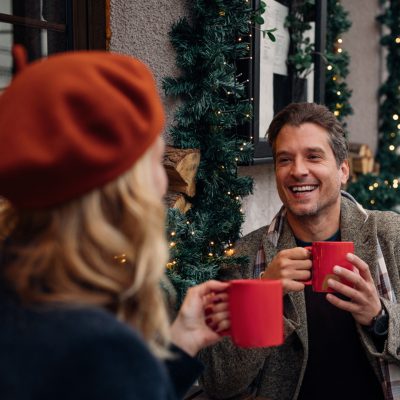 Smiling man and unrecognizable woman sitting in a cafe decorated for Christmas season and laughing together