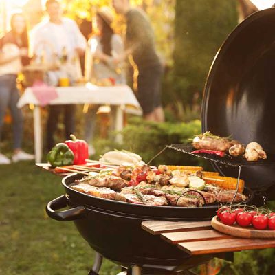 Group of friends having party outdoors. Focus on barbecue grill with food. Space for text
